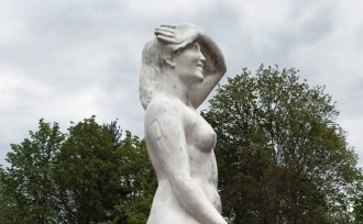Rzeźba nagiej, uśmiechniętej kobiety na tle drzew ("Jutrzenka" Zofii Trzcińskiej-Kamińskiej)