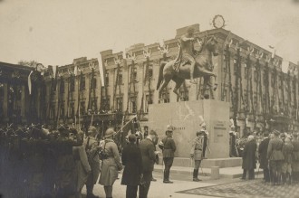 Fotografia. W centrum pomnik księcia Józefa Poniatowskiego, w tle przystrojony Pałac Saski. Na pierwszym planie żołnierze i cywile oddający hołd monumentowi.